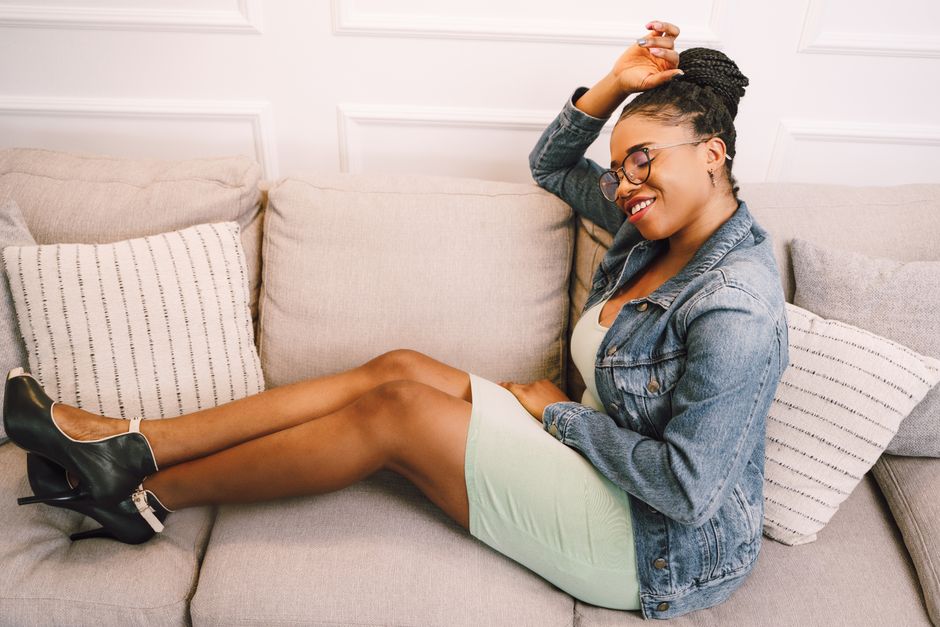 Stylish woman in a jean jacket lounging on a couch with a joyful expression, embodying modern casual fashion.