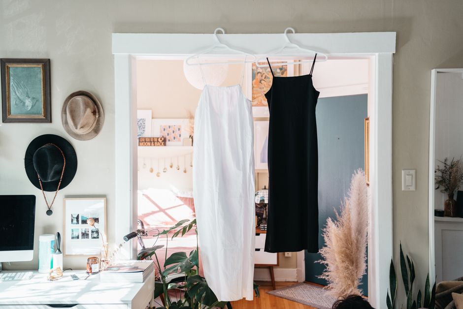 Bright interior showcasing black and white dresses hanging in a doorway with hats on the wall.