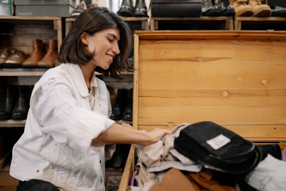 A young woman smiles as she sorts through clothes in a vintage store's wooden box.