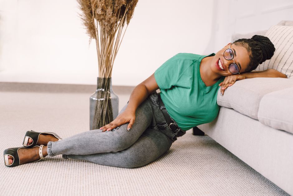 Chic fashion portrait of a smiling woman in glasses lounging on a sofa.