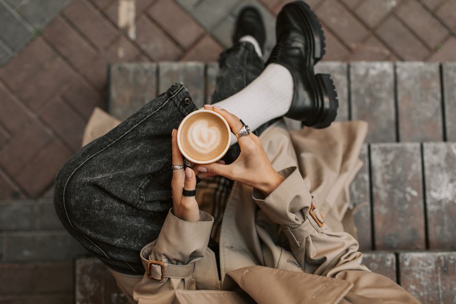 A person sitting on steps holding a latte art coffee cup, showcasing style and relaxation.