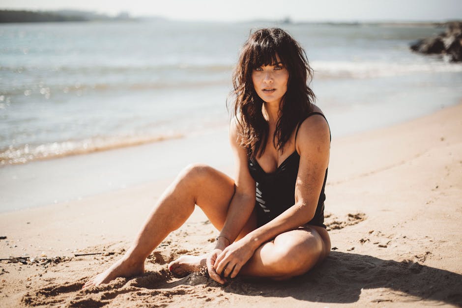 Brunette woman enjoying a sunny day at the beach, sitting on the sand near the sea.