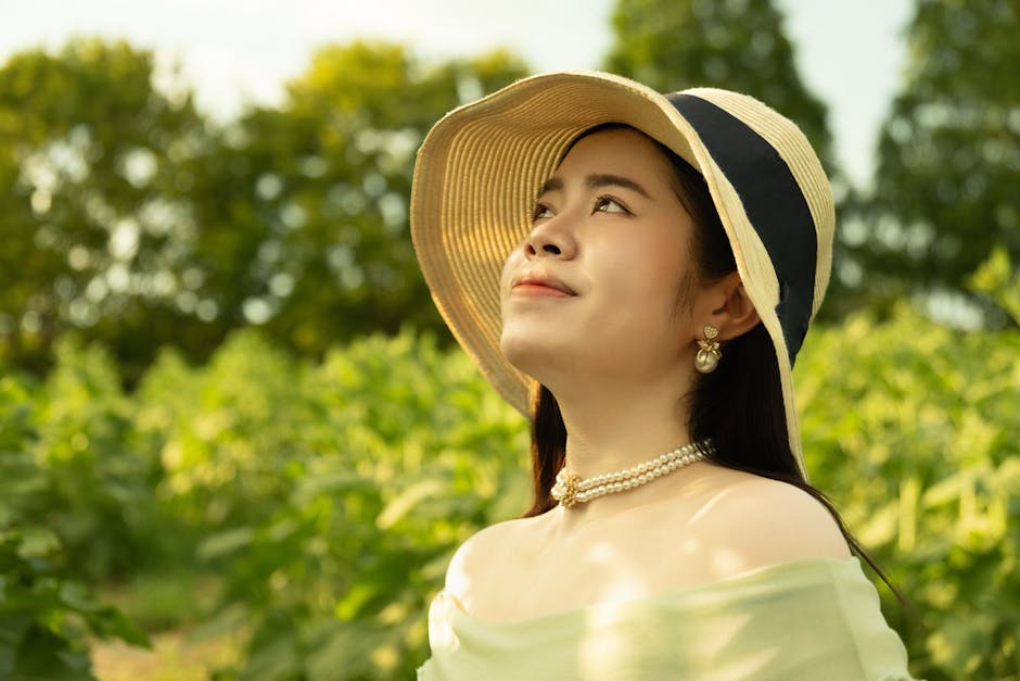 Woman wearing a summer hat smiles in a green field, enjoying the warm sunshine.