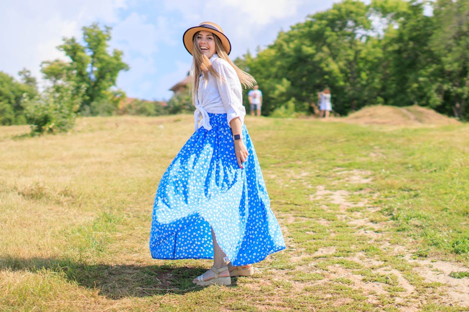 Woman with hat and blue skirt smiling in a sunny park setting. Summer vibes.