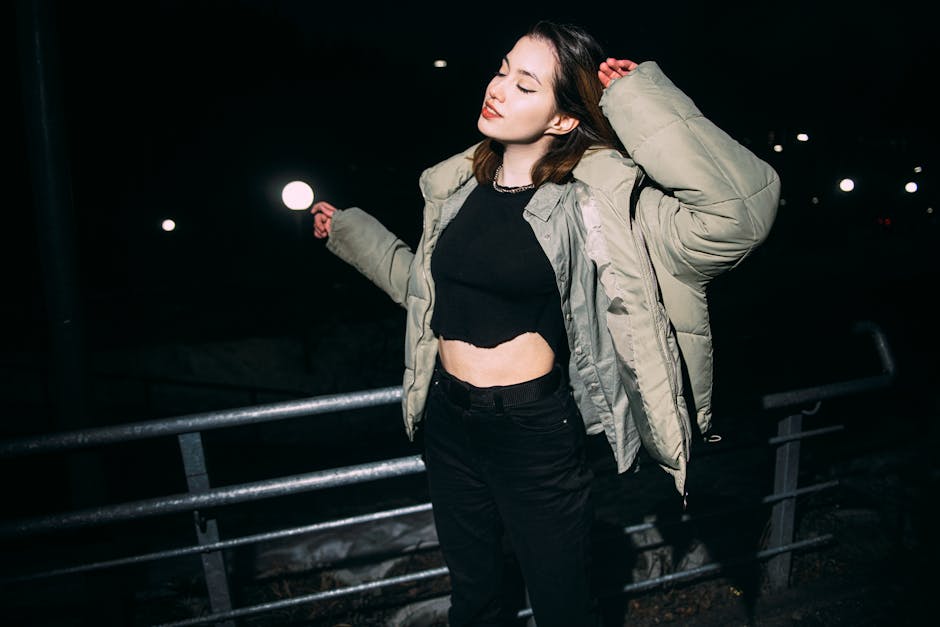 Woman with eyes closed posing confidently at night, wearing a green winter jacket in urban setting.