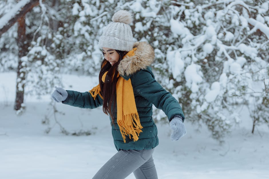 A young woman in winter attire runs joyfully through a snowy forest, smiling warmly.