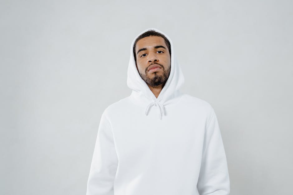 Portrait of a young adult man wearing a white hoodie against a minimalistic background.