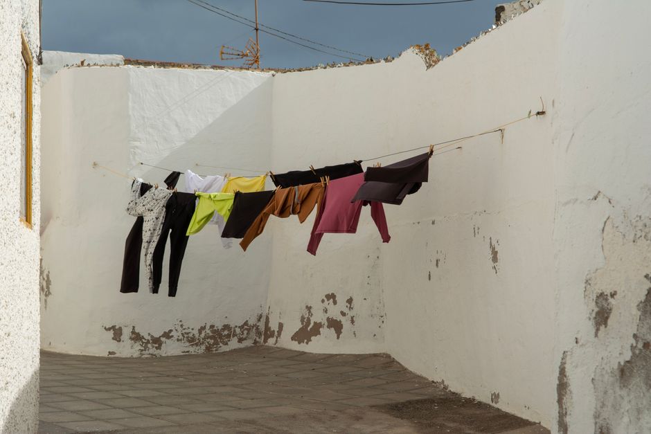 Colorful clothes drying on a clothesline against a rustic white wall outdoors, capturing urban simplicity.