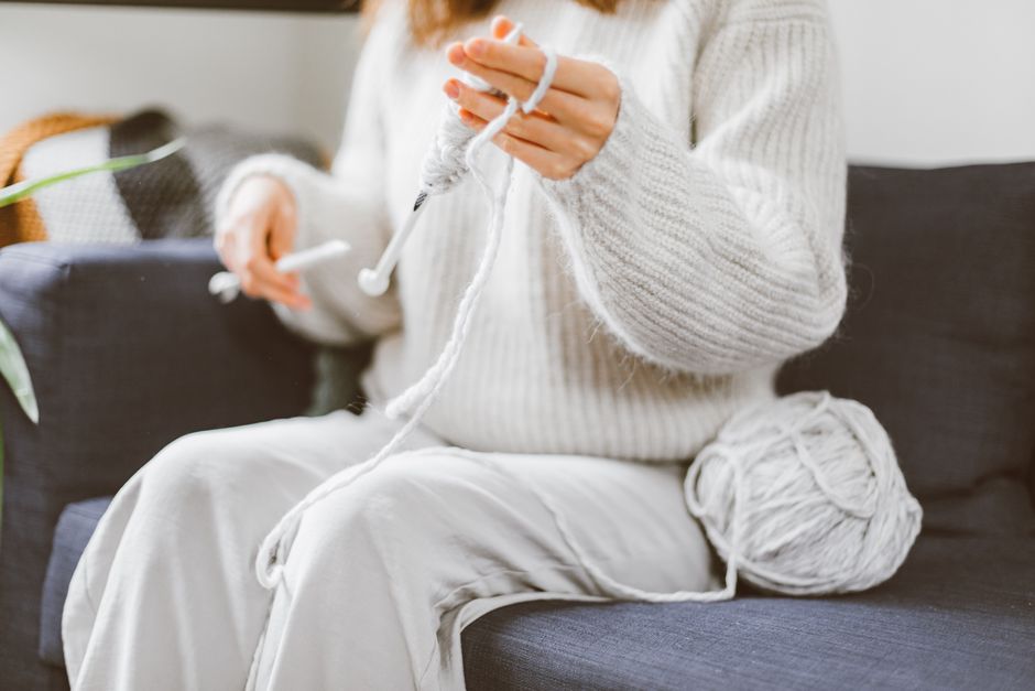 Close-up of a person knitting with white yarn on a cozy indoor couch, showcasing a hobby.