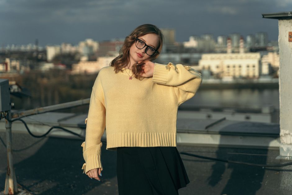 Young woman posing in a yellow sweater on a rooftop in Minsk, Belarus, with cityscape in the background.