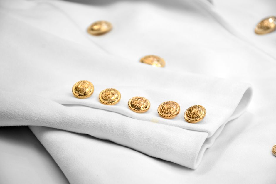 Close-up image of a stylish white jacket featuring detailed gold buttons in a fashion-forward setting.