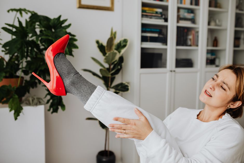 A woman indoors, trying on striking red high heels, showcasing a fashion-forward moment.