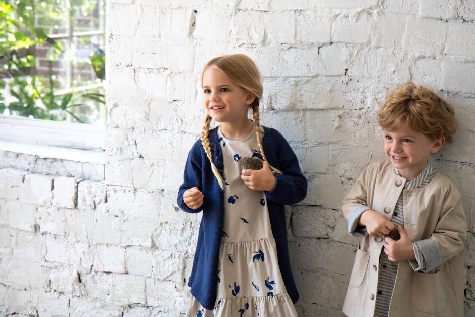 Two cheerful children smiling indoors against a white brick wall.