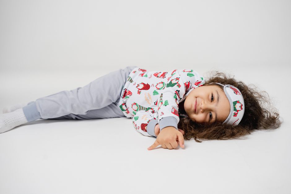 Adorable child with brown hair in festive pajamas lying on a white background, smiling warmly.