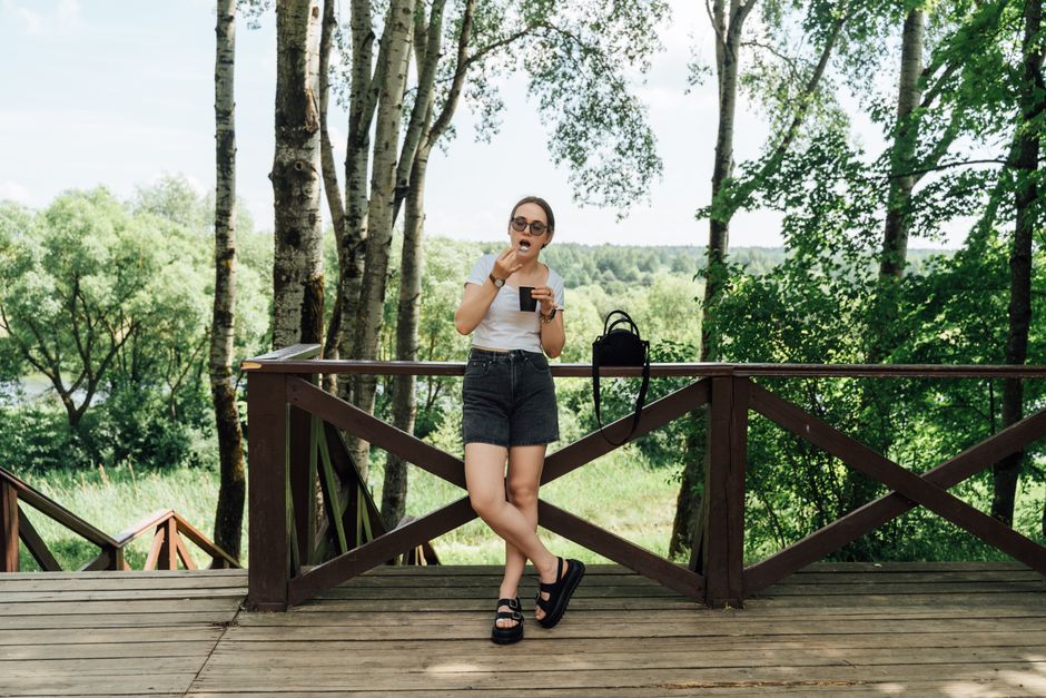 Young woman enjoys ice cream on a sunny summer day on a wooden patio surrounded by lush greenery.