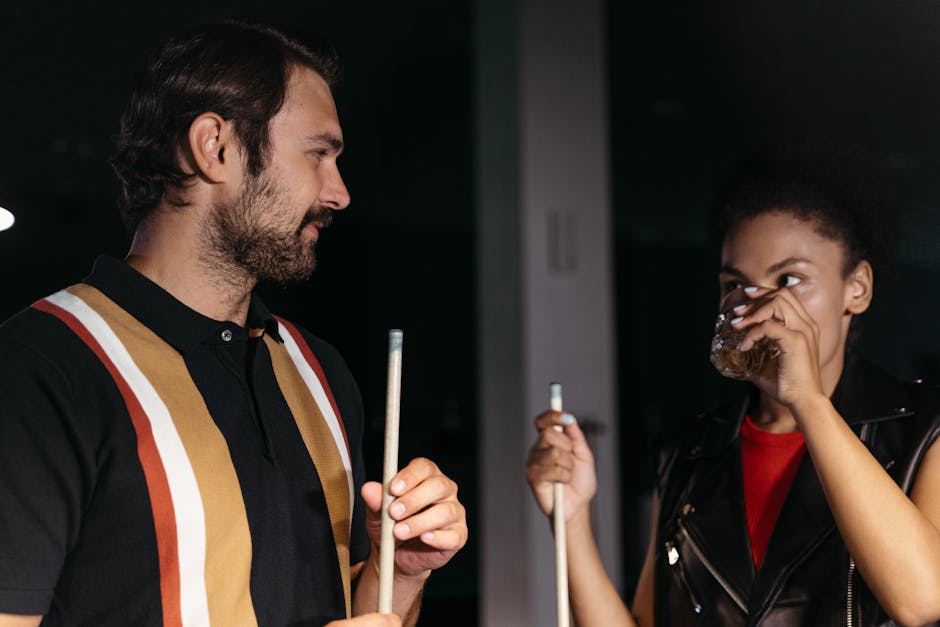 A man and woman socializing over billiards, holding cue sticks and drinks.