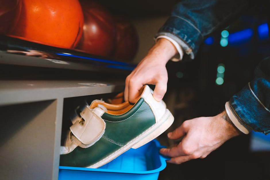 Close-up of hands handling bowling shoes with bowling balls in the background.