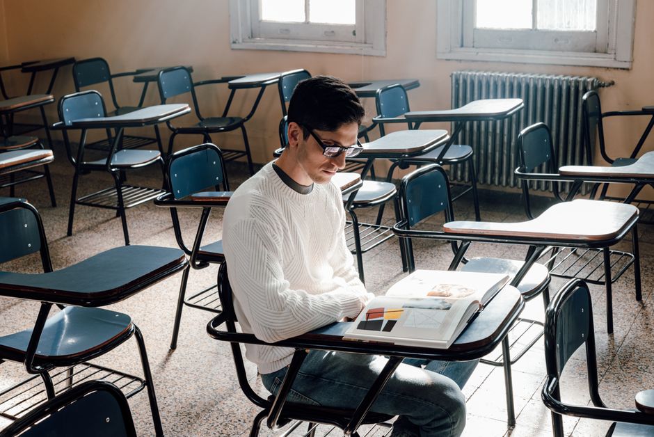 A lone student reading in an empty classroom with sunlight streaming through windows.
