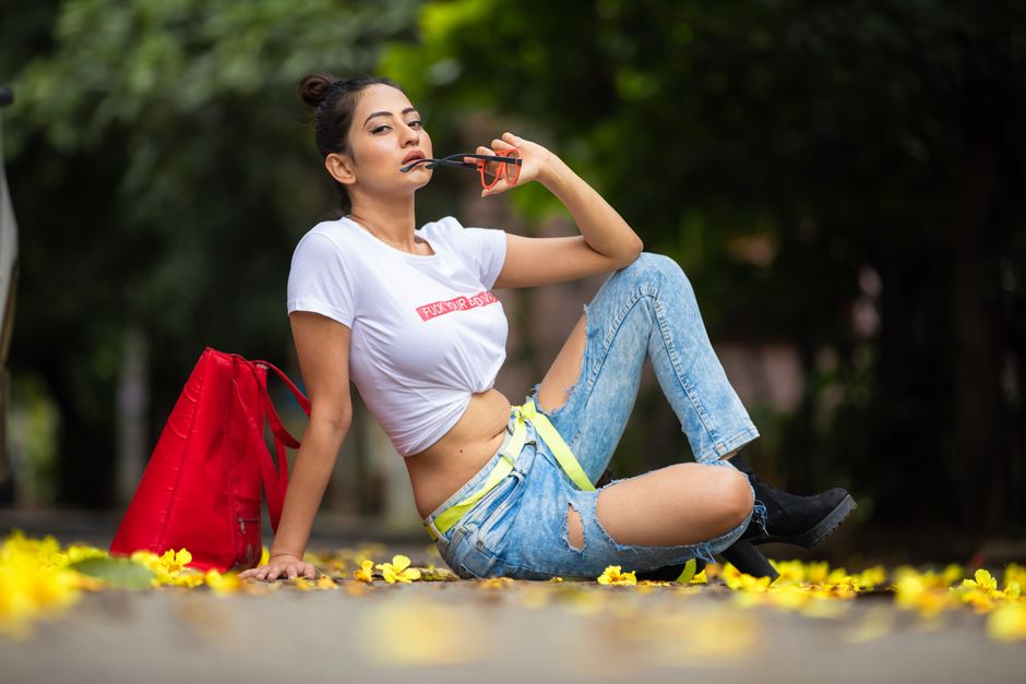 Model in trendy casual attire posing outdoors, surrounded by yellow blooms.