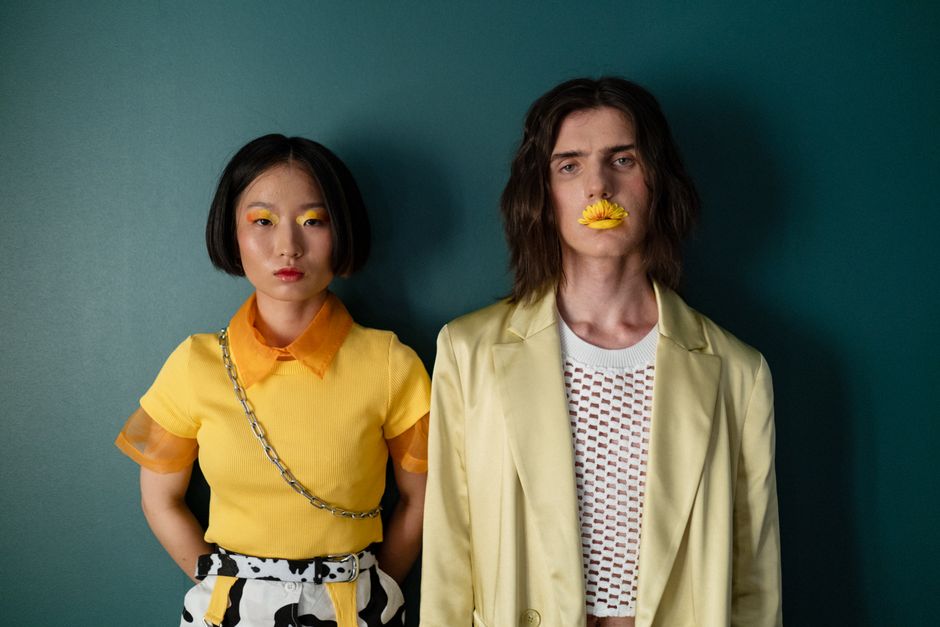 Stylish portrait of two young adults posing with bold outfits against a green background.