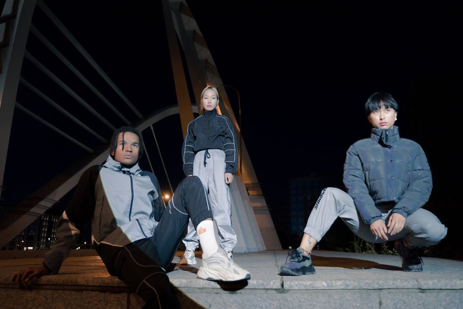 Stylish group in urban fashion poses on a modern bridge at night, exuding a trendy vibe.