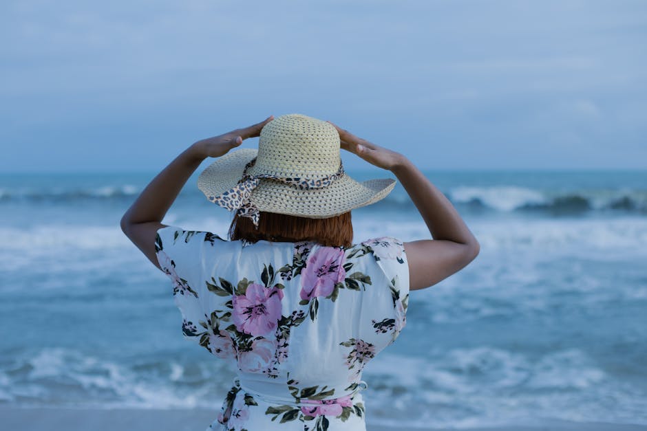 Woman enjoying a peaceful day at the tropical beach, wearing a sun hat and floral dress.