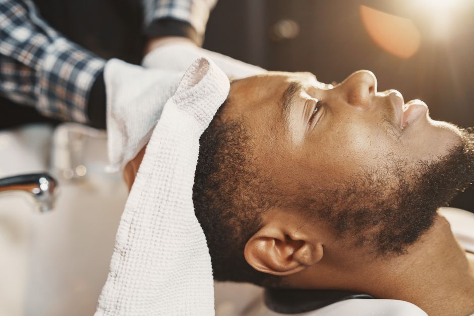 Close-up of a man enjoying a relaxing moment with a towel at a barbershop.