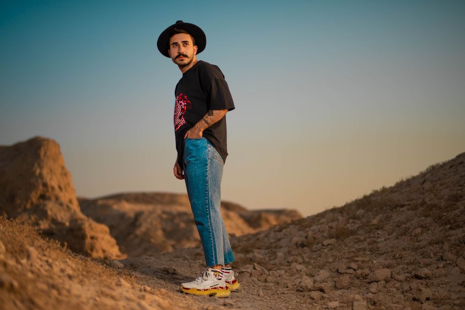Portrait of a young man in casual attire standing outdoors on rocky terrain at sunset.