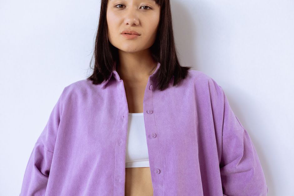 Young woman in a purple button down shirt posing confidently with a white backdrop.