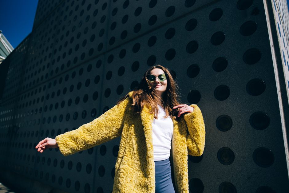 Stylish woman wearing a yellow fur coat poses confidently outdoors in daylight.