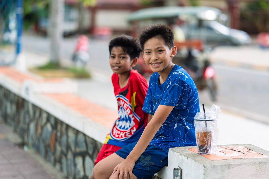 Two cheerful boys sitting on a street ledge, enjoying a sunny day outside, with blurred urban background.