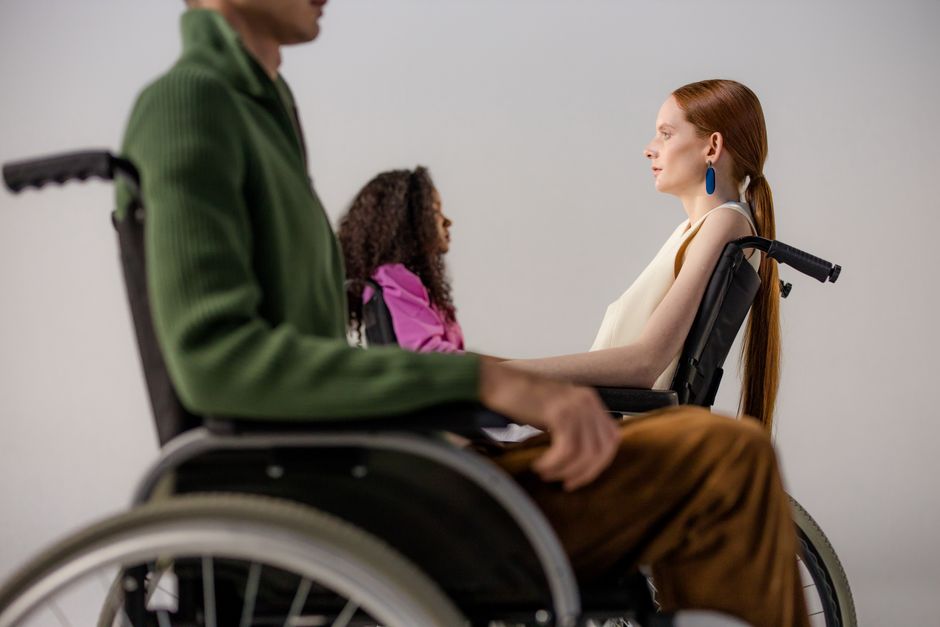 Group of diverse individuals posing in wheelchairs during a studio fashion shoot, showcasing stylish clothing.