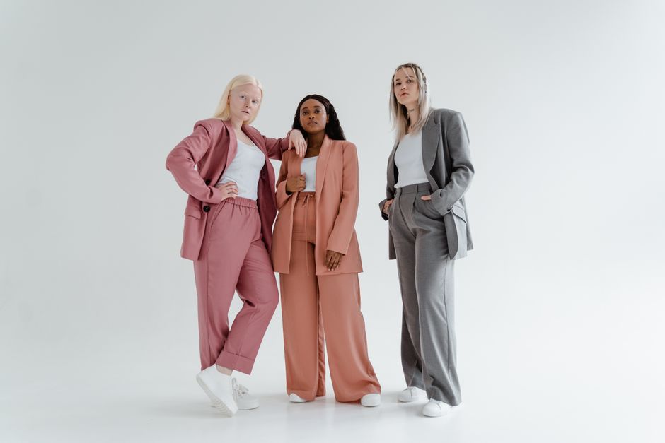 Three diverse women in stylish suits exuding confidence, standing against a white studio background.