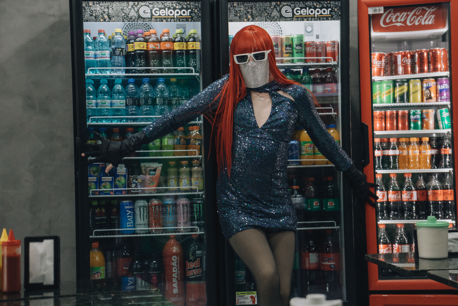 Fashionable individual in a sequined outfit posing confidently by drink coolers.