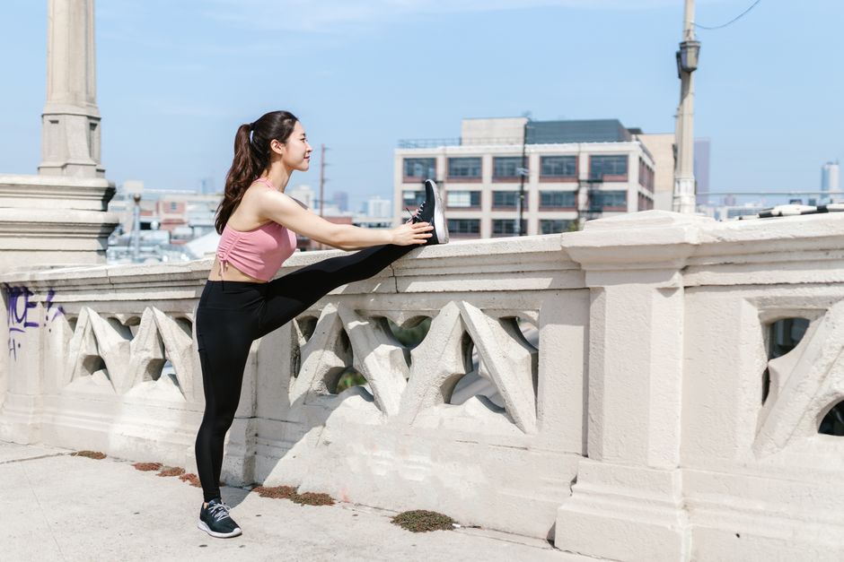 Woman in athletic wear stretching her leg on a city bridge railing, ideal for fitness themes.