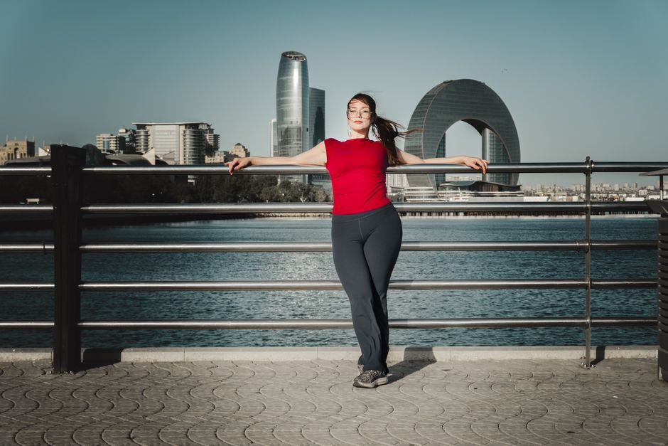 Woman leaning on railing with modern skyline behind at a waterfront location.