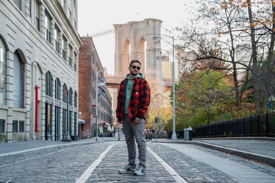 A man stands in Brooklyn's street with the iconic Brooklyn Bridge in the background.