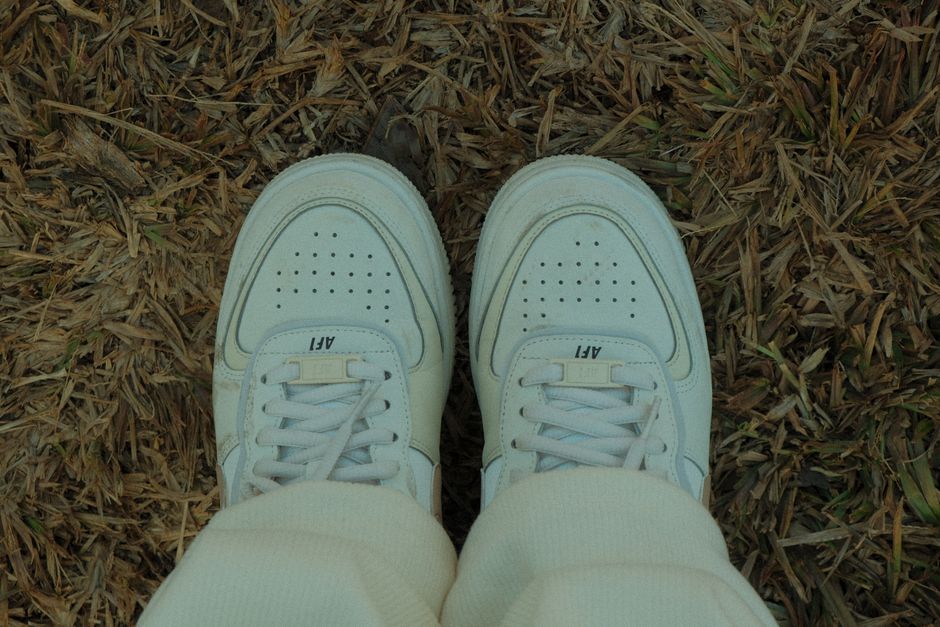 Top-view photo of white sneakers on dry grass, showcasing casual footwear style.