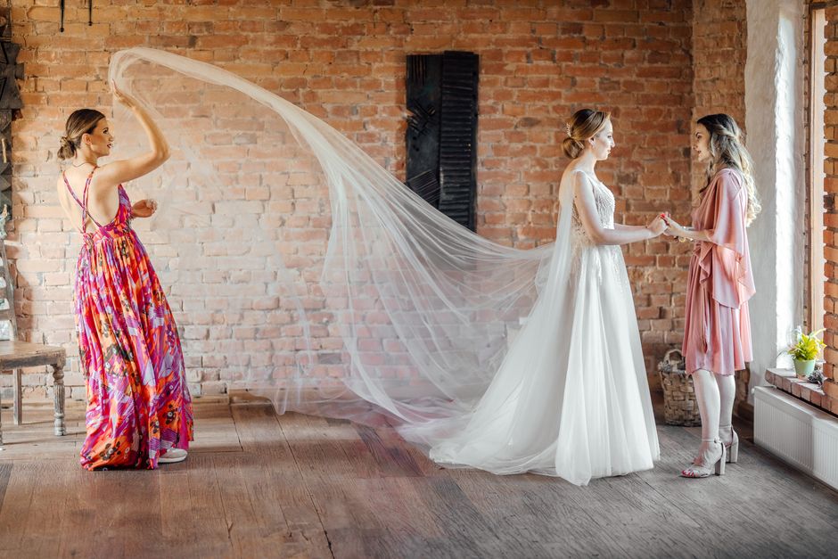 A bride in a wedding dress with bridesmaids in a rustic indoor setting, sharing a joyful moment.