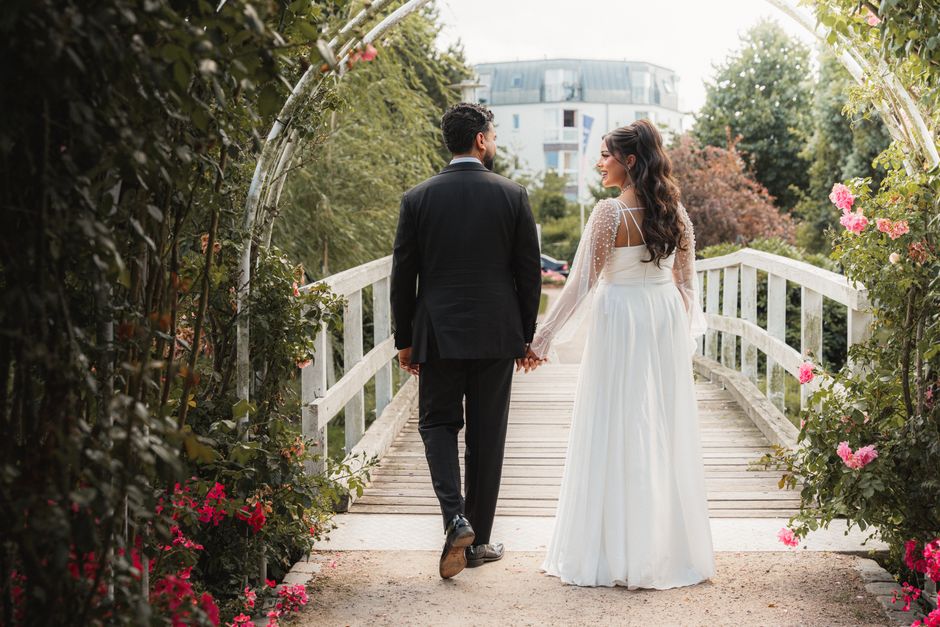 Bride and groom walking hand-in-hand through a lush garden bridge in Hamburg.