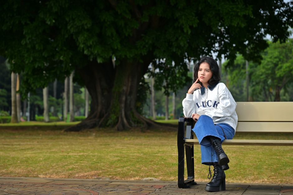 Young woman sitting on a bench in a vibrant park setting. Casual and thoughtful mood.