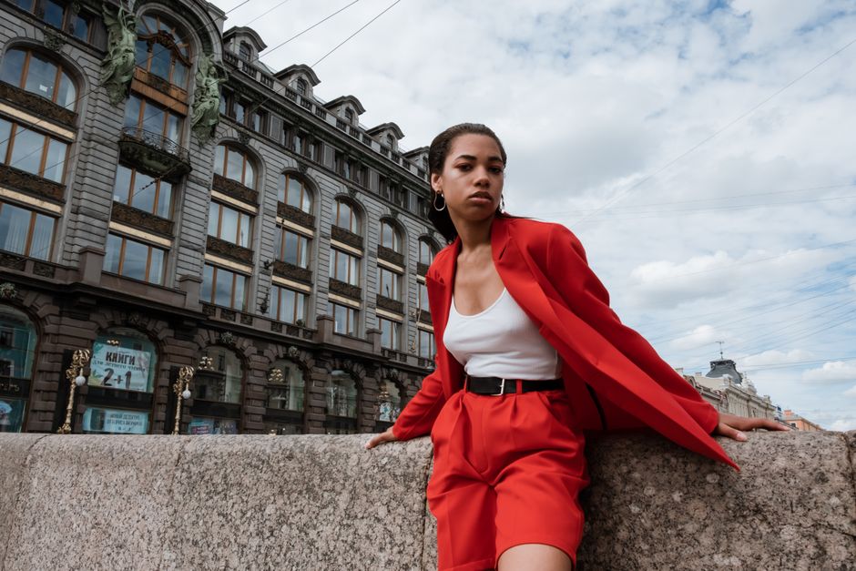 Stylish woman poses confidently in a vibrant red suit by a historical building in Saint Petersburg.