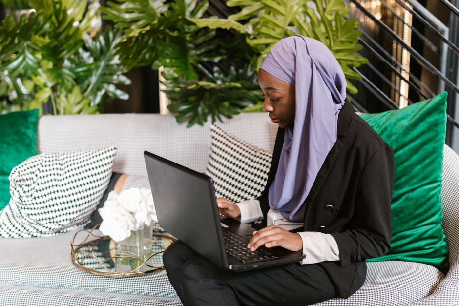Professional woman in a hijab working on a laptop in a stylish office setting.