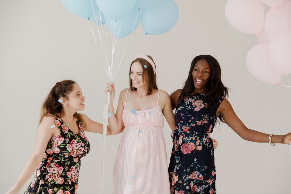 Three women holding balloons, smiling, and celebrating indoors against a light backdrop.