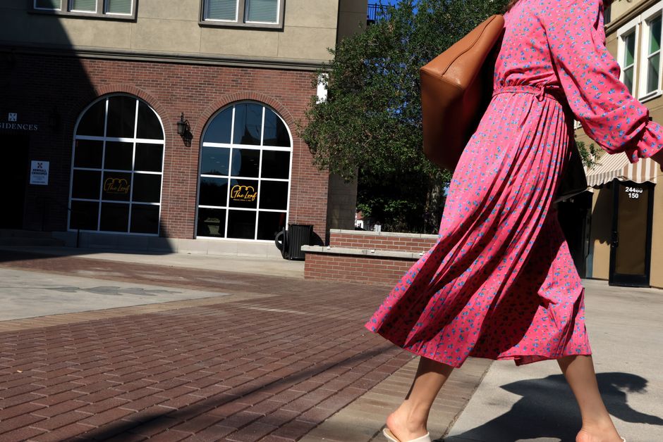 A woman in a pink floral dress walking, capturing fashion and movement in a sunny urban environment.