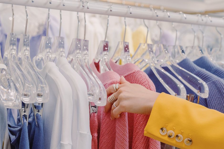 Close-up of a shopper selecting colorful sweaters on a clothes rack in a boutique.