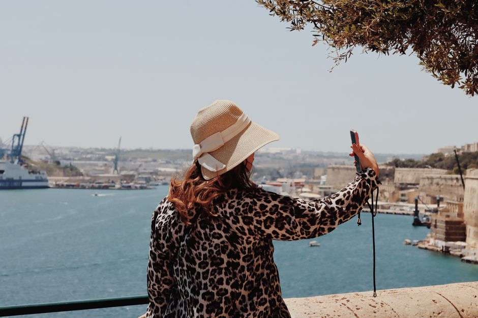 A woman takes a selfie overlooking the stunning harbor of Valletta, Malta under the bright summer sun.