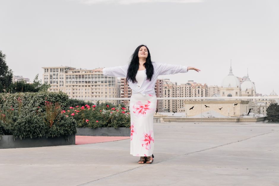 Woman enjoys a peaceful moment with arms outstretched in a city garden.