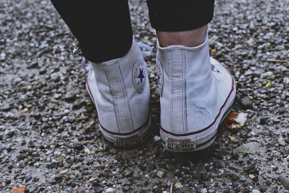 Stylish white high-top sneakers on a gravel surface, showcasing fashion and wear.