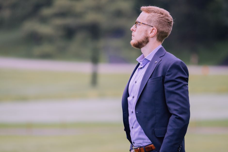 Side profile of a businessman in a suit standing outdoors with a blurred green background.